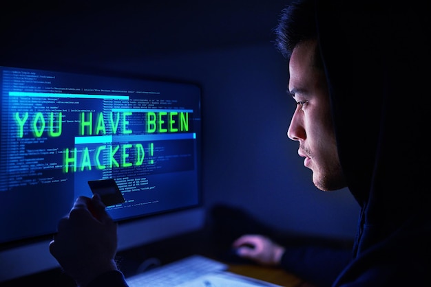 Su dinero es mío ahora Disparo de un pirata informático encapuchado que usa una computadora en la oscuridad