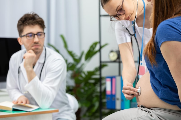 Foto su médico ausculta el abdomen de una paciente embarazada con un estetoscopio