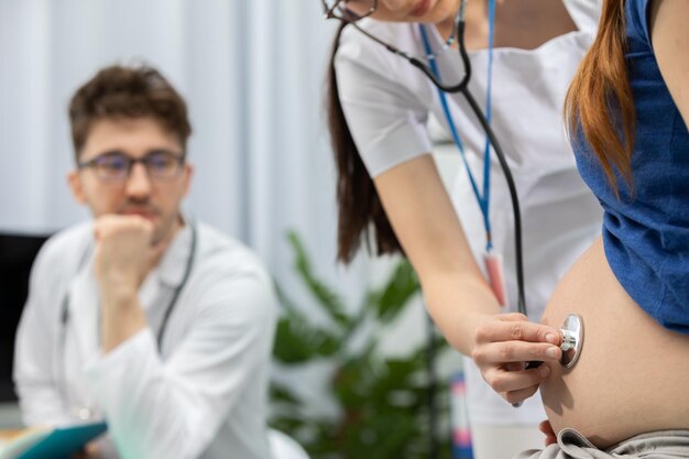 Foto su médico ausculta el abdomen de una paciente embarazada con un estetoscopio