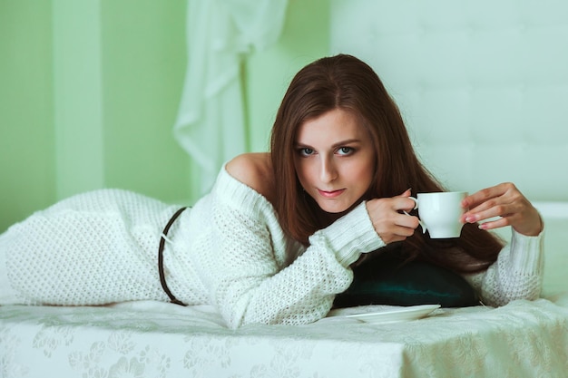 Suave retrato de mujer joven sentada en la cama en casa