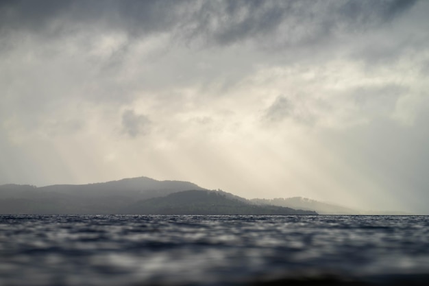 suaves y hermosos rayos sobre el agua a través de nubes sobre una isla al amanecer con nubes rosadas y el océano debajo