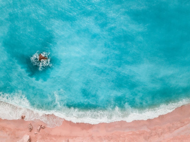 Las suaves olas azules del mar con espuma blanca en la playa de arena tonifican el moderno color coral vivo del año 2019 disparado desde un dron.