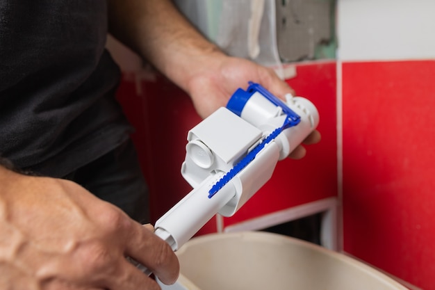 Substituição de peças de tanques sanitários. Um homem com luvas laranja conserta o ralo do tanque do vaso sanitário.