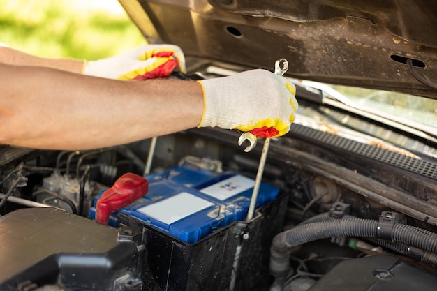 Substituição e reparo da bateria Um mecânico de automóveis remove uma bateria de carro sob o capô de um carro para substituição ou carregamento