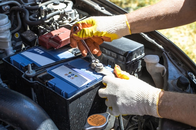 Substituindo a bateria em um carro O mecânico desaparafusa os prendedores da bateria com uma chave de fenda