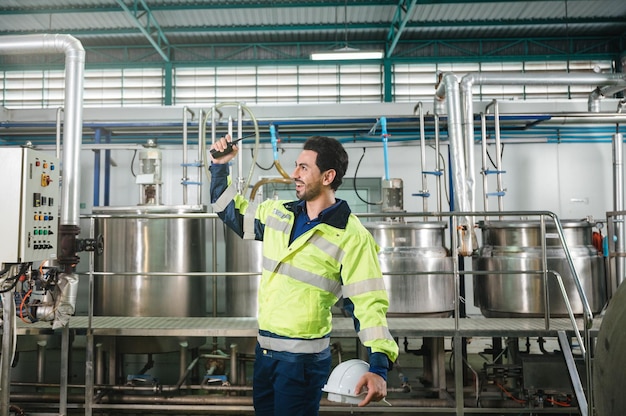 Sucesso do engenheiro técnico caucasiano em uniforme de segurança em pé no laboratório de tanque de caldeira de tubulação na planta de processamento de bebidas