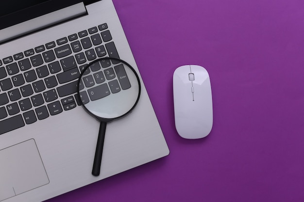 Suchinformation. Laptop mit PC-Maus, Lupe auf lila Hintergrund. Ansicht von oben