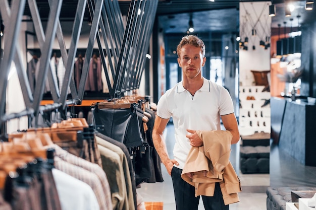 Sucht nach Jacke Junger Mann in modernem Geschäft mit neuer Kleidung Elegante, teure Kleidung für Männer