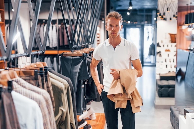 Sucht nach Jacke Junger Mann in modernem Geschäft mit neuer Kleidung Elegante, teure Kleidung für Männer