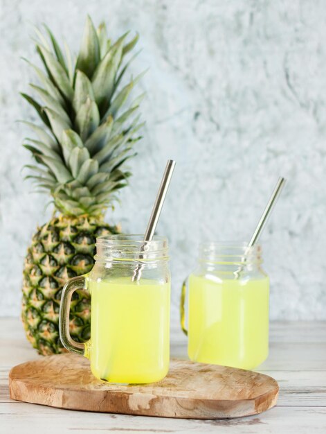 Foto suco de abacaxi em frascos de vidro de pedreiro com canudos e frutas de abacaxi na placa de madeira