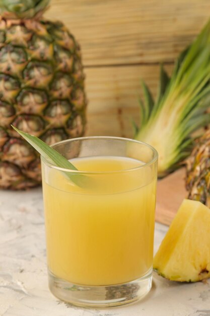 Foto suco de abacaxi em um copo e pedaços de abacaxi fresco em um fundo de madeira natural frutas de verão