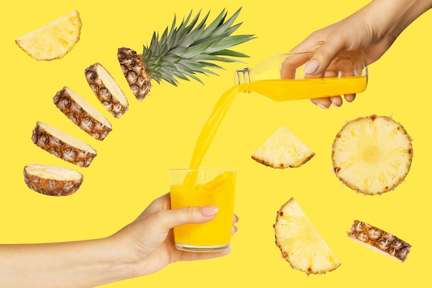 Suco de abacaxi fresco é derramado de uma garrafa em um copo mãos femininas Abacaxis voadores pedaços de abacaxi em um fundo amarelo Conceito