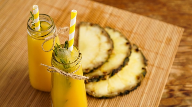 Suco de abacaxi fresco feito com gelo em uma pequena garrafa de vidro com fundo de madeira. Bebida caseira.