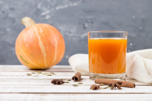 Suco de abóbora em vidro sobre uma mesa de madeira. especiarias em paus de canela e anis estrelado. fundo cinza