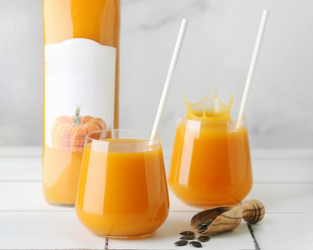 Suco de abóbora fresco em vidro na mesa de luz com sementes de abóbora e a garrafa de suco perto. conceito de comida saudável e saborosa. Colheita de outono.