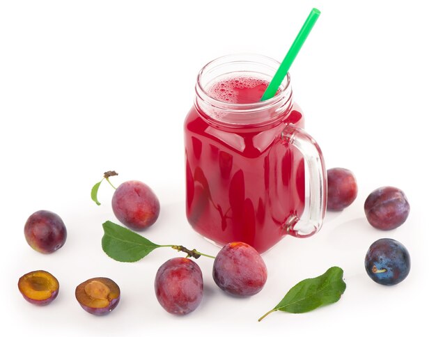 Suco de ameixa em um copo com frutas frescas de ameixa, isolado no fundo branco.