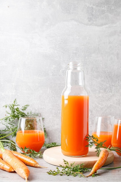 Suco de cenoura em um copo e garrafa e cenouras frescas com folhas