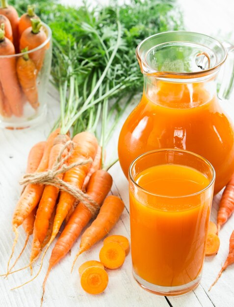 Foto suco de cenoura em vidro e jarro e cenouras frescas em fundo de madeira