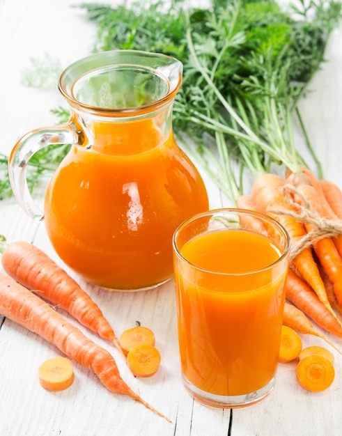 Suco de cenoura em vidro e jarro e cenouras frescas