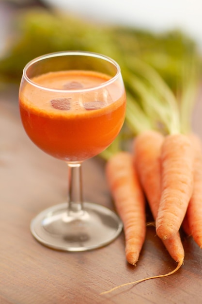 Suco de cenoura vegetal e comida saudável com arte colorida e criatividade para menu nutricionista Bebida vegana em vidro para dieta de bem-estar ou nutrição em uma mesa de madeira com ingredientes