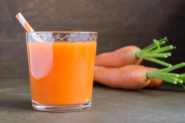 Suco de cenouras maduras frescas em um fundo marrom.