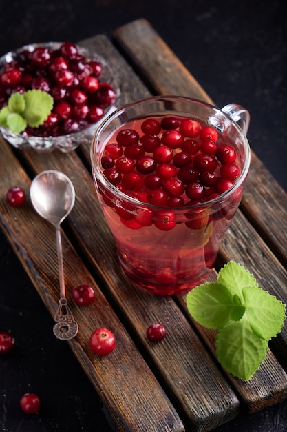 Foto suco de cranberry com mel em um copo, cranberries em açúcar. em uma mesa de madeira escura