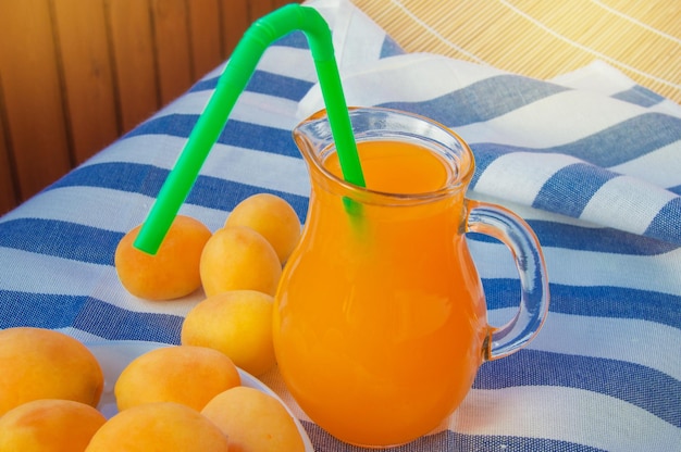 Suco de damasco de bebida de verão em uma jarra de vidro com palha e frutas em um guardanapo listrado em um verão ensolarado