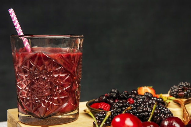 Suco de desintoxicação de frutas vermelhas em vidro cortado com um canudo ao lado de alguns maduros