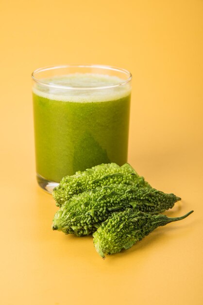 Suco de ervas de cabaça amarga ou Karela é o melhor remédio natural para diabetes. Melões amargos inteiros e um copo cheio de suco guardados sobre um fundo colorido ou de madeira. Foco seletivo