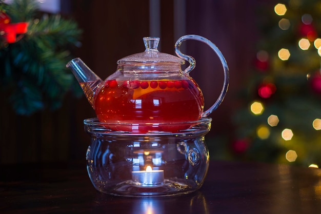 Suco de fruta quente em um bule transparente com uma vela no fundo da decoração de Reveillon.