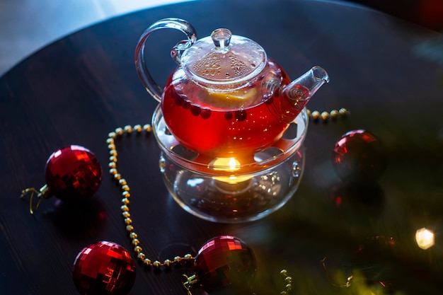 Suco de fruta quente em um bule transparente com uma vela no fundo da decoração de Reveillon.