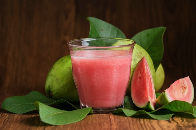 Suco de goiaba vermelha é servido em um fundo de madeira com fatias de goiaba e enfeites de folhas