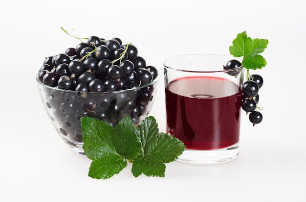 Suco de groselha preta em vidro e frutas maduras em copo de vidro com folhas verdes em um fundo branco