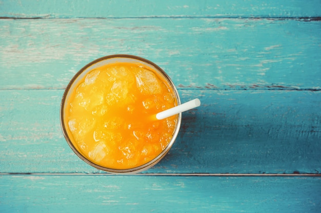 Suco de laranja da vista superior no vidro com gelo no conceito de madeira das horas de verão do azul de oceano.