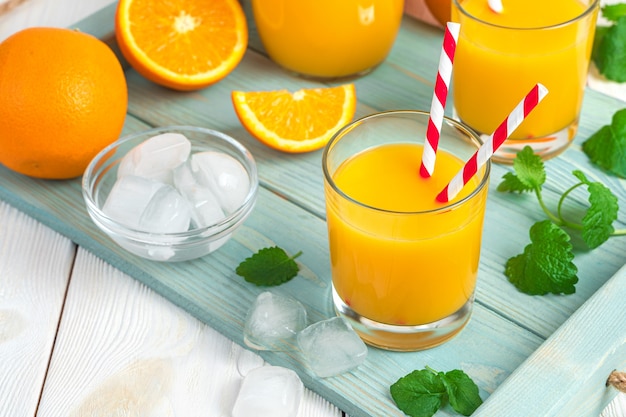 Suco de laranja em copos com tubos em uma mesa de hortelã e laranjas. visão horizontal