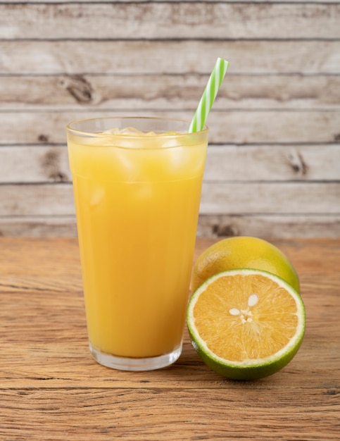 Suco de laranja em um copo com gelo e frutas sobre a mesa de madeira.