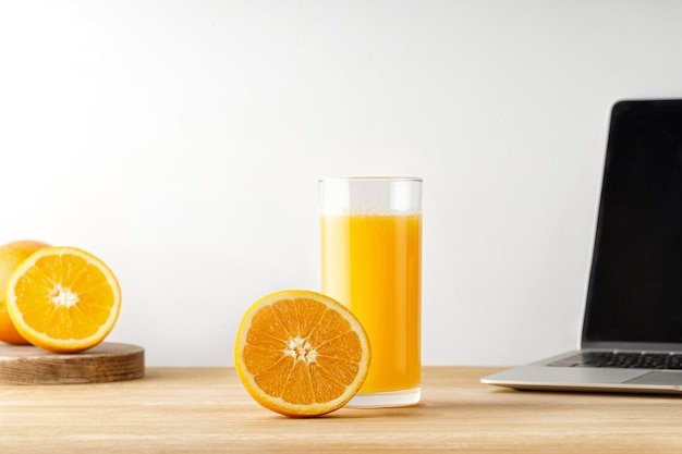 Suco de laranja em um copo com meia laranja cortada na mesa de madeira com laptop Vitamina C Trabalhando em casa