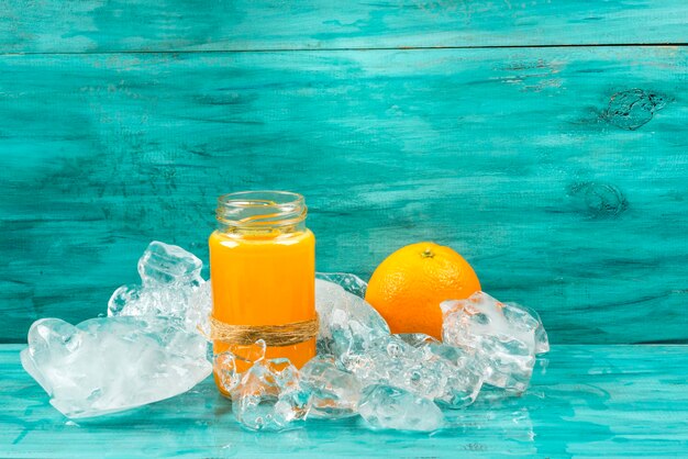 Suco de laranja em vidro com laranja no gelo sobre fundo azul, copie o espaço.
