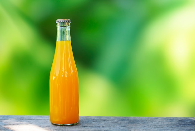 Suco de laranja embalado em garrafas de vidro tampo da mesa feita de madeira e verde natureza fundo