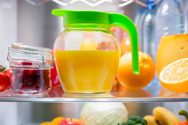 Suco de laranja espremido na hora em uma jarra e frutas na prateleira da geladeira