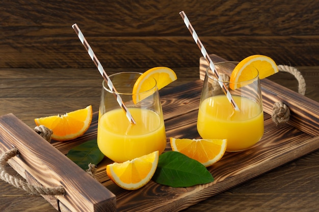 Suco de laranja fresco em copos com laranjas cortadas na bandeja de madeira. Natureza morta rústica com frutas cítricas.