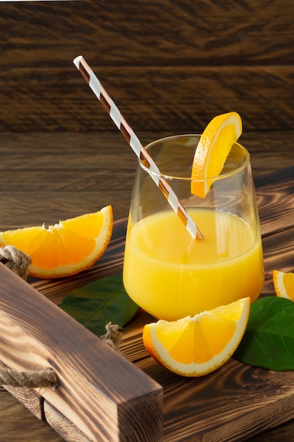 Suco de laranja fresco em copos com laranjas cortadas na bandeja de madeira. Natureza morta rústica com frutas cítricas.