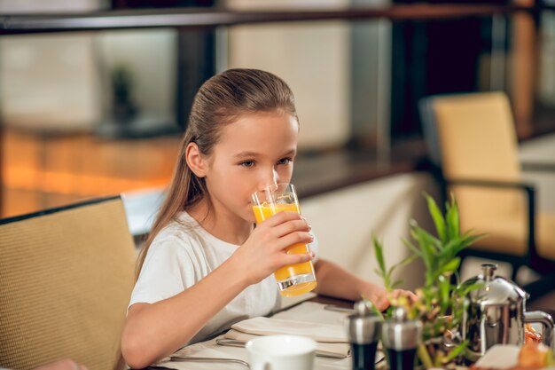 Suco de laranja. linda garota sentada à mesa bebendo suco de laranja