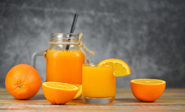 Suco de laranja na jarra de vidro e fatia de frutas frescas de laranja na mesa de madeira