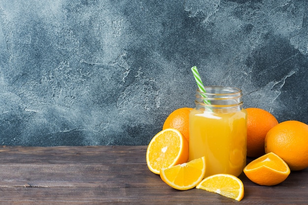 Suco de laranja no frasco de vidro e nas laranjas das frutas frescas no fundo escuro com espaço da cópia.