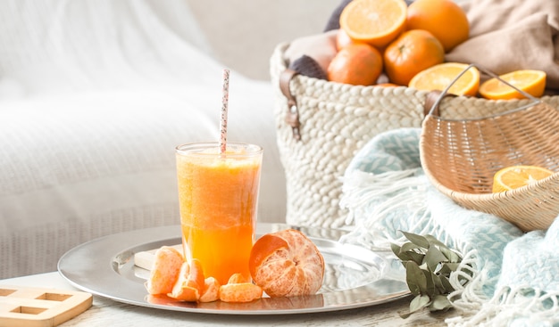 Suco de laranja orgânico fresco cultivado no interior da casa, com um cobertor turquesa e uma cesta de frutas