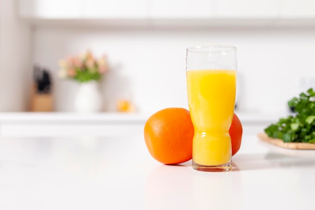 suco de laranja recém-espremido em um copo fica perto de laranjas em uma cozinha moderna branca comida saudável