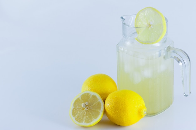 Suco de limão com gelo em uma jarra de vidro decorado com rodelas de limão com cubos de limão cortados ao meio sobre um fundo branco