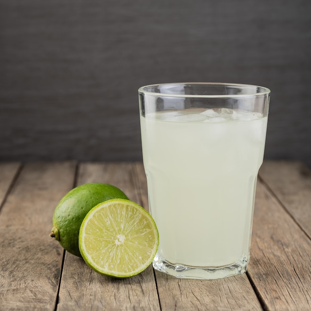 Foto suco de limão verde em um copo com frutas sobre a mesa de madeira.