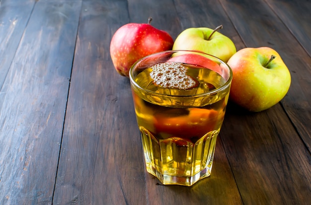 Suco de maçã em um copo e uma maçã madura em uma mesa de madeira